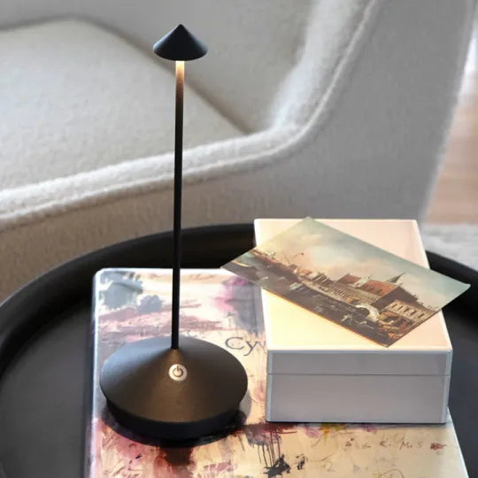 Schwarze LED-Tischlampe auf rundem Tisch, modernes Design, neben weißer Box und Postkarte.