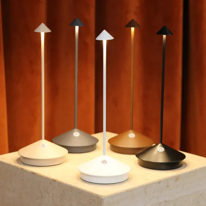 Moderne LED-Tischlampen in verschiedenen Farben auf einem Podest vor braunem Hintergrund.
